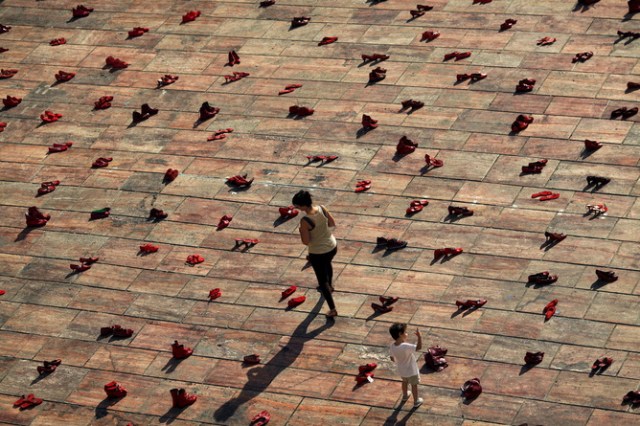 A woman and a child walk amidst an art installation of 745 pairs of female red shoes, put on display by Mexican visual artist Elina Chauvet to protest against gender violence and femicide, at La Constitucion Square in Malaga